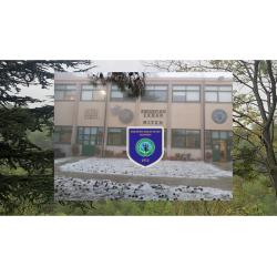 Το σήμα του σχολείου και η φωτογραφία της πρόσοψης του σχολείου μια χιονισμένη μέρα. Πίσω η βλάστηση που περιβάλλει το σχολείο.